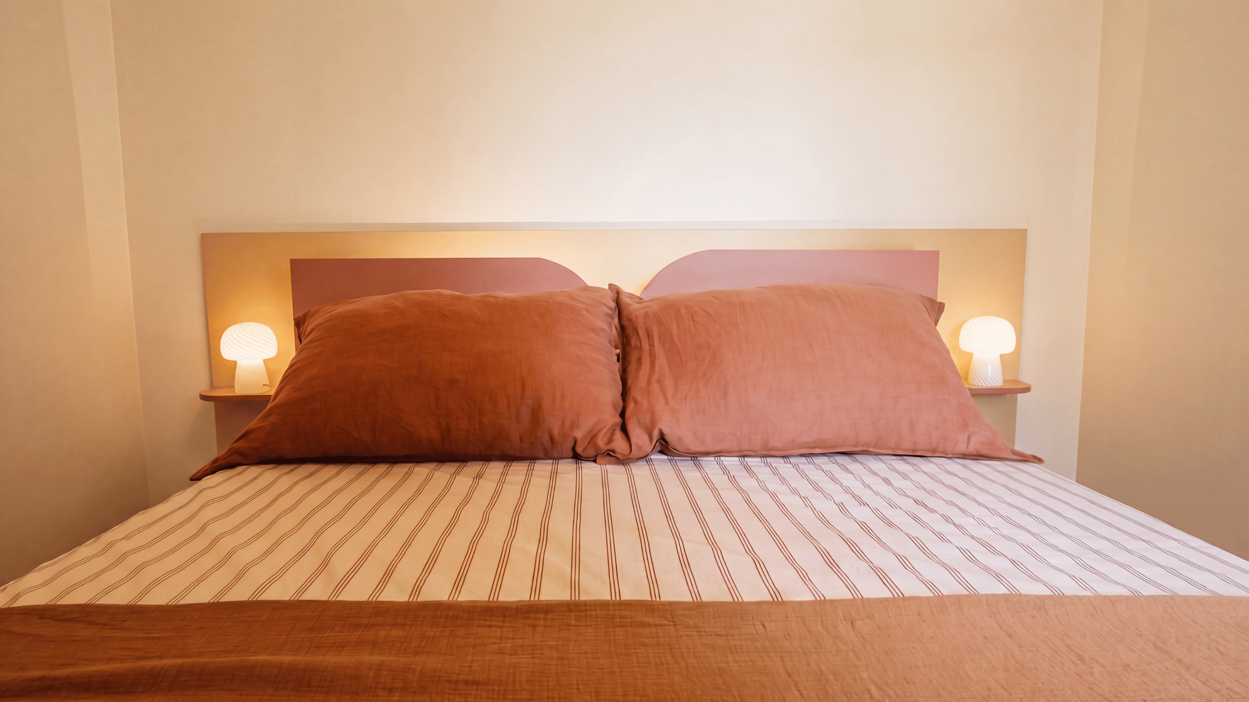 Lit double avec tête de lit sur mesure en bois, liseuses intégrées et linge de lit en teintes terracotta dans une maison d'architecte à Vannes.