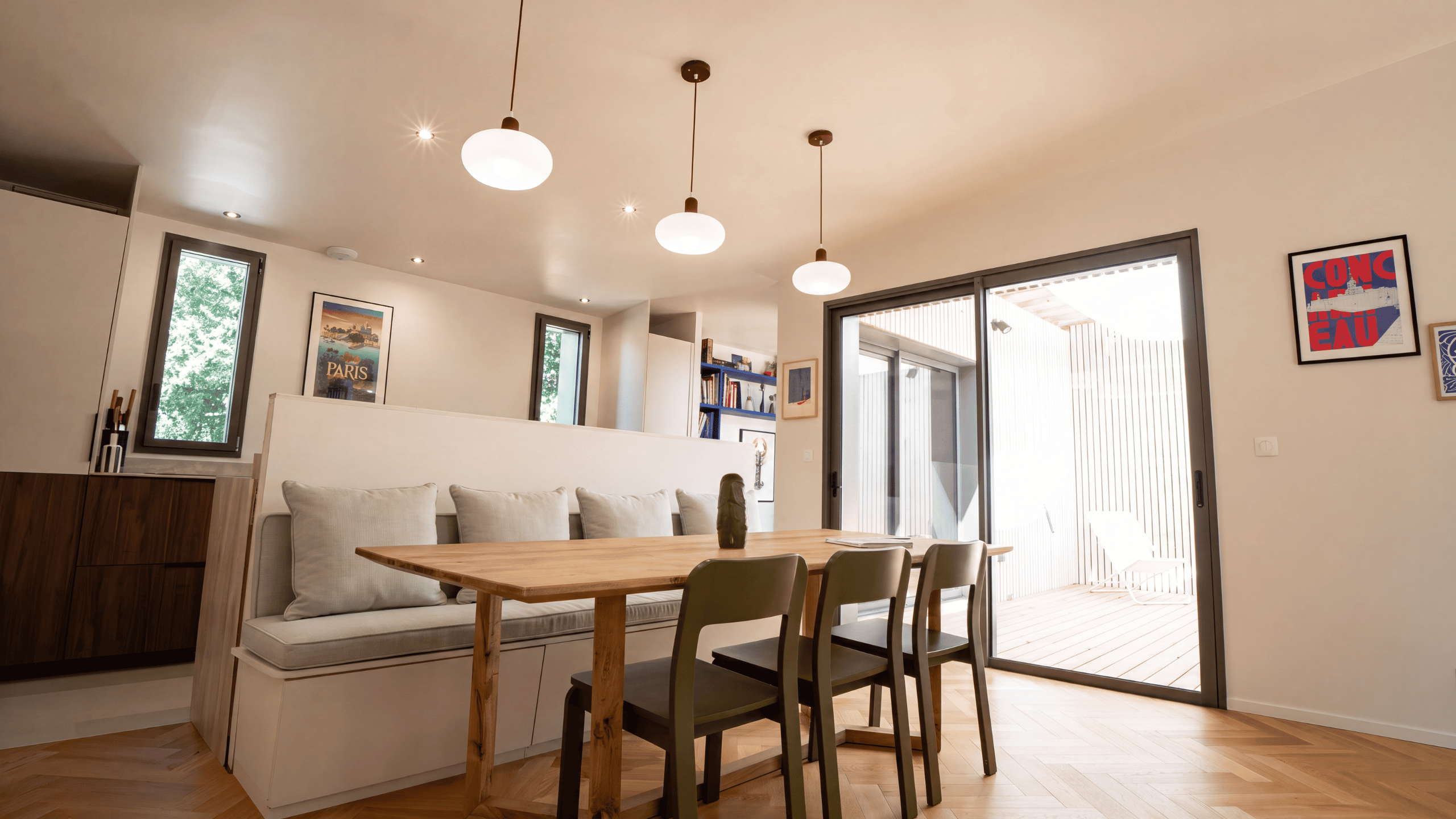 Espace salle à manger lumineux avec banquette sur mesure, table en bois et baies vitrées coulissantes dans une maison d'architecte à Vannes.