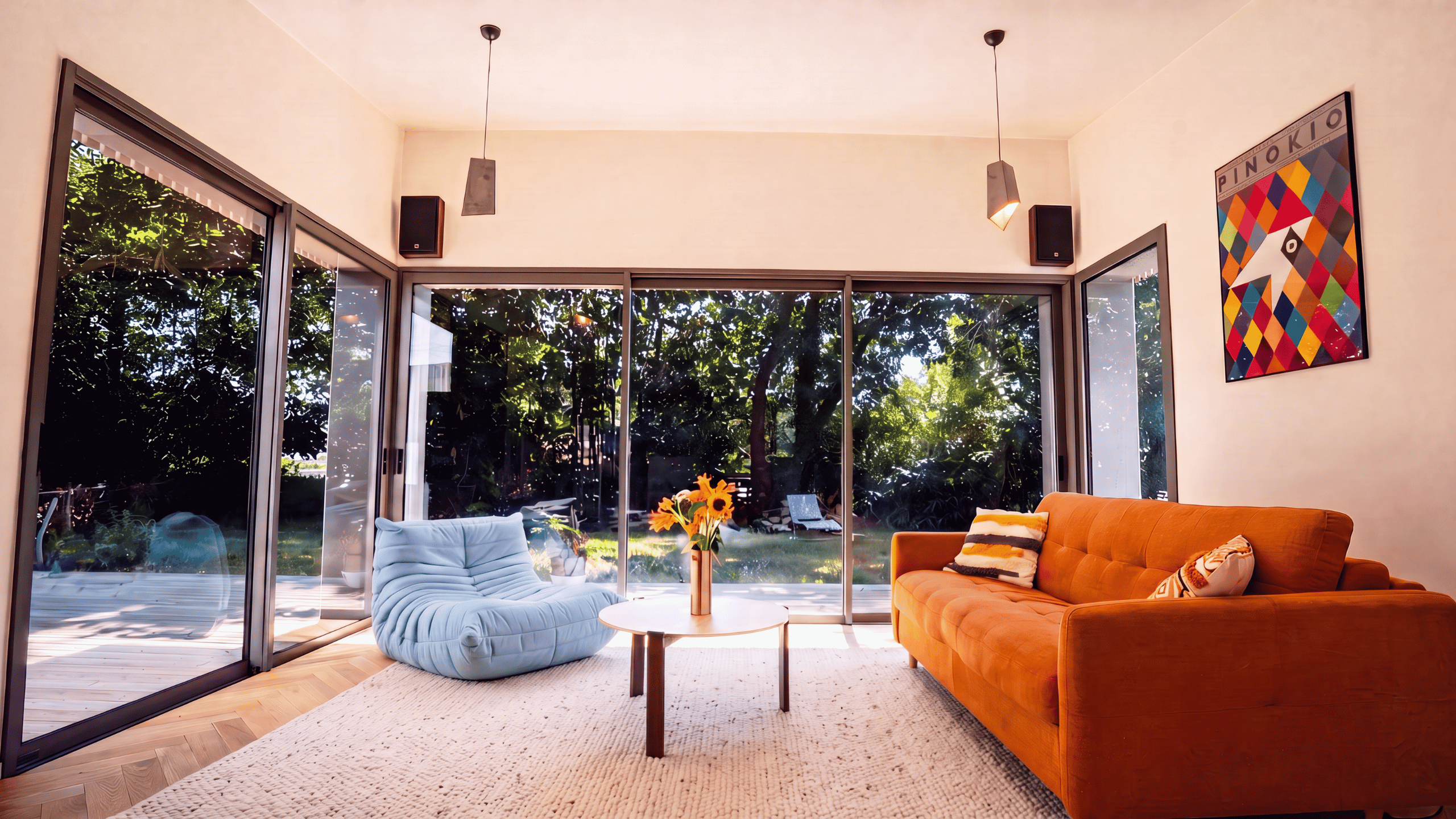Grand salon lumineux d'une maison d'architecte à Vannes avec canapé orange, fauteuils bleus et baies vitrées donnant sur la verdure.