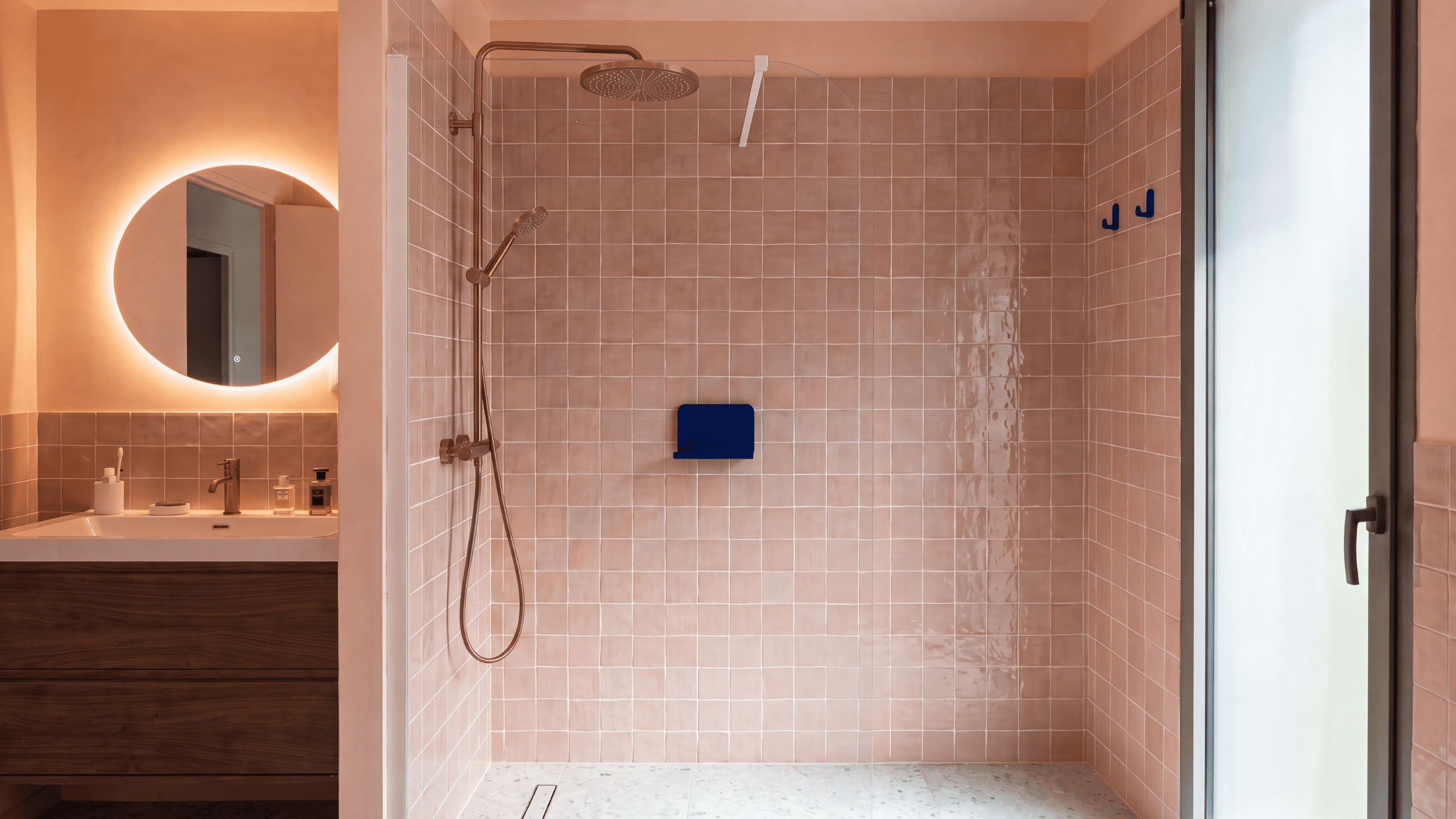 Espace baignoire et douche dans une salle de bain rose avec miroir rond rétroéclairé dans une maison d'architecte à Vannes.