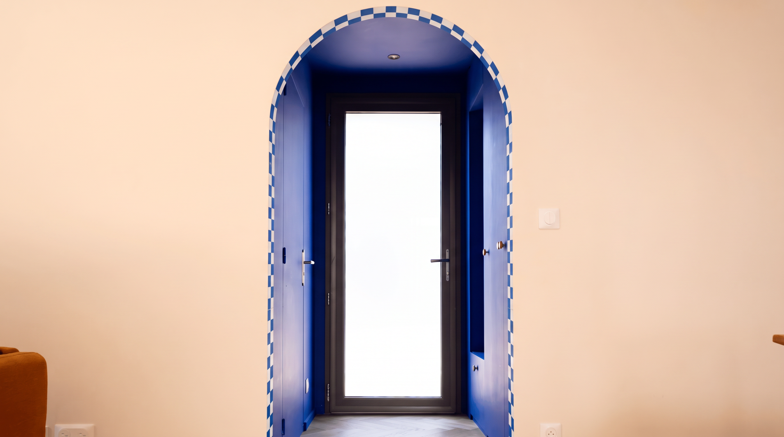 Couloir d'une maison d'architecte à Vannes avec une ouverture en arche bleue donnant sur une porte vitrée lumineuse.